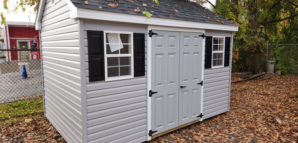 a-frame shed with gray siding and double doors, and two windows with black shutters